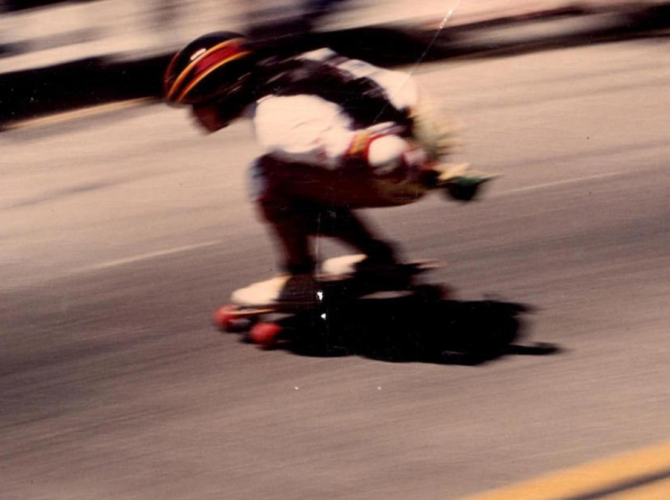 Woman skateboarding on a street, passing a blurred crowd of people.